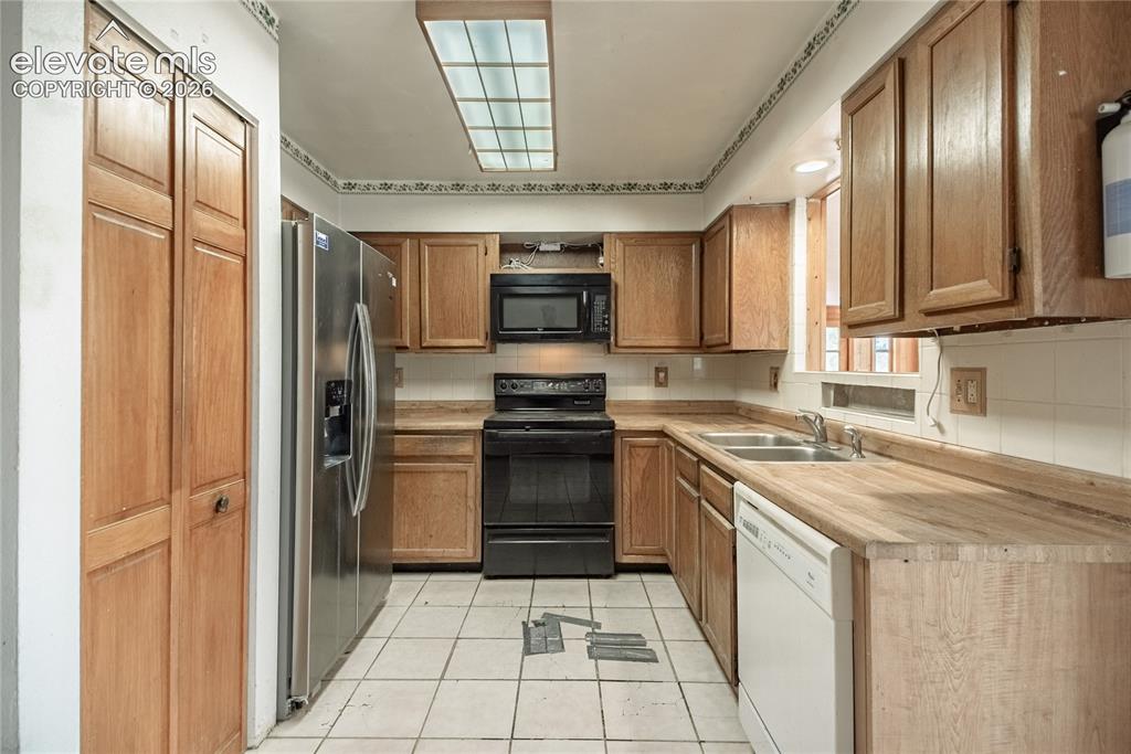 Image 12 of 50: Kitchen with wood cabinetry, tile flooring, and a stainless steel refrigera