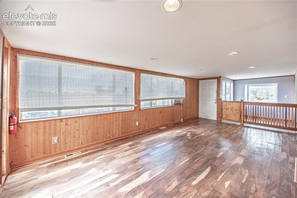 Image 20 of 50: Wood-finish flooring, paneled wood walls, and multiple windows with blinds
