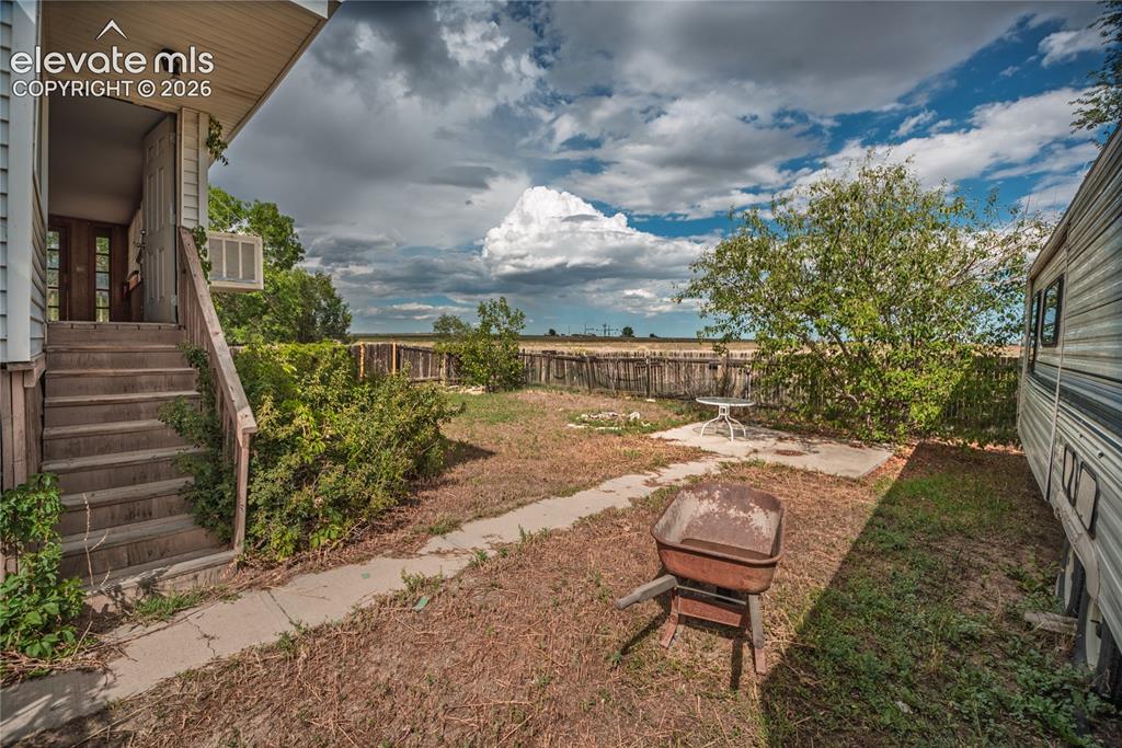 Image 44 of 50: Rear exterior with wooden staircase entry, concrete patio area, and mature 