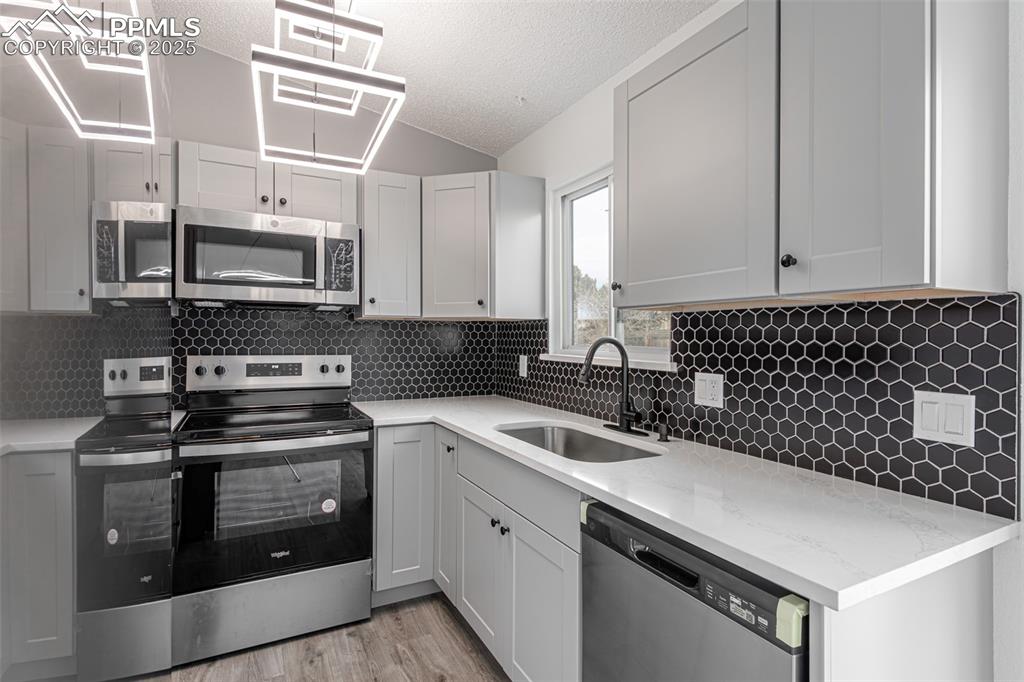 Image 11 of 33: Kitchen with a textured ceiling, backsplash, a sink, light wood-style floor