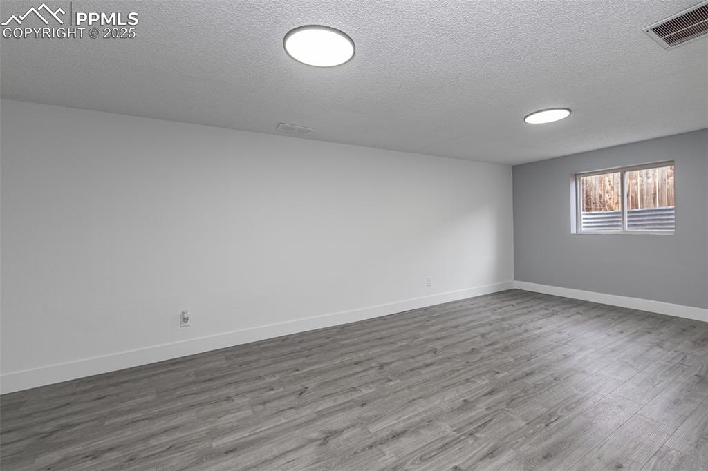 Image 19 of 33: Empty room with baseboards, visible vents, wood finished floors, and a text