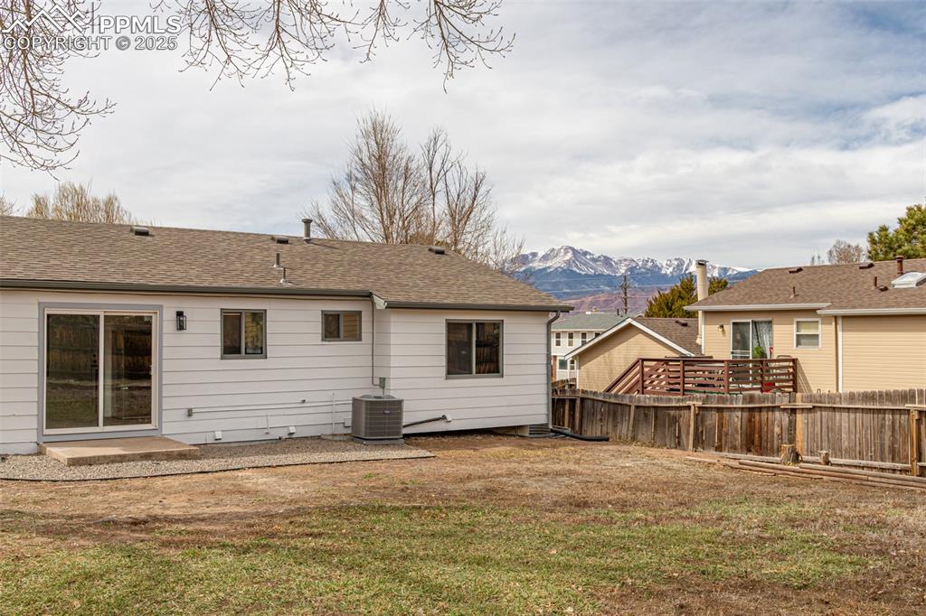 Image 25 of 33: Back of house featuring cooling unit, roof with shingles, fence, a mountain