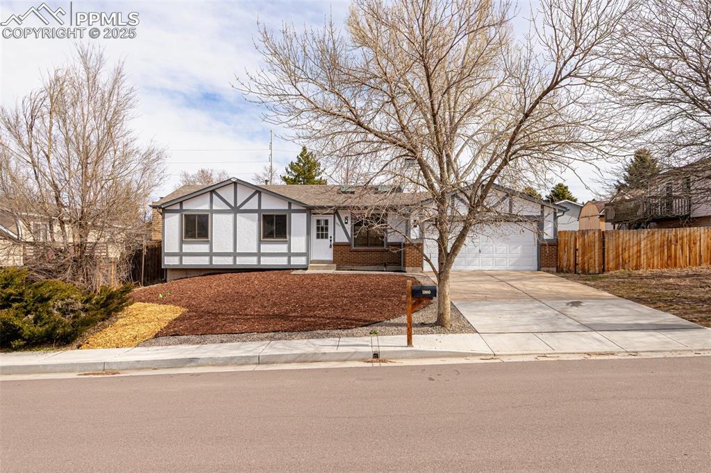 Image 3 of 33: View of front facade with brick siding, driveway, fence, and a garage