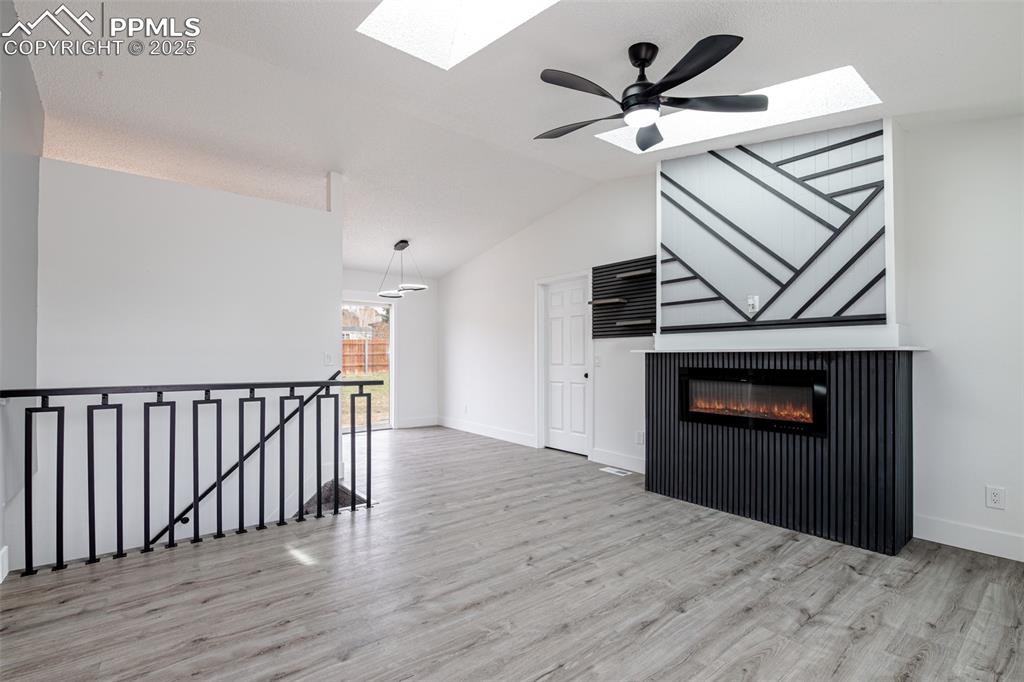 Image 5 of 33: Unfurnished living room with baseboards, vaulted ceiling with skylight, cei