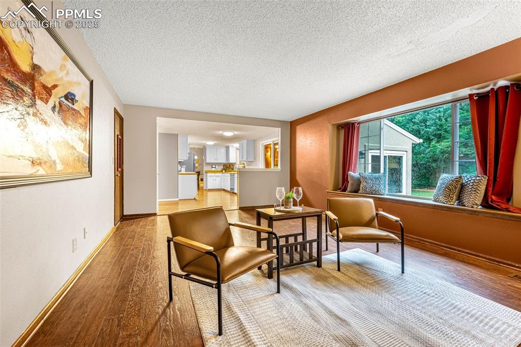 Image 12 of 40: Living area featuring light wood-type flooring, a textured ceiling, and bas