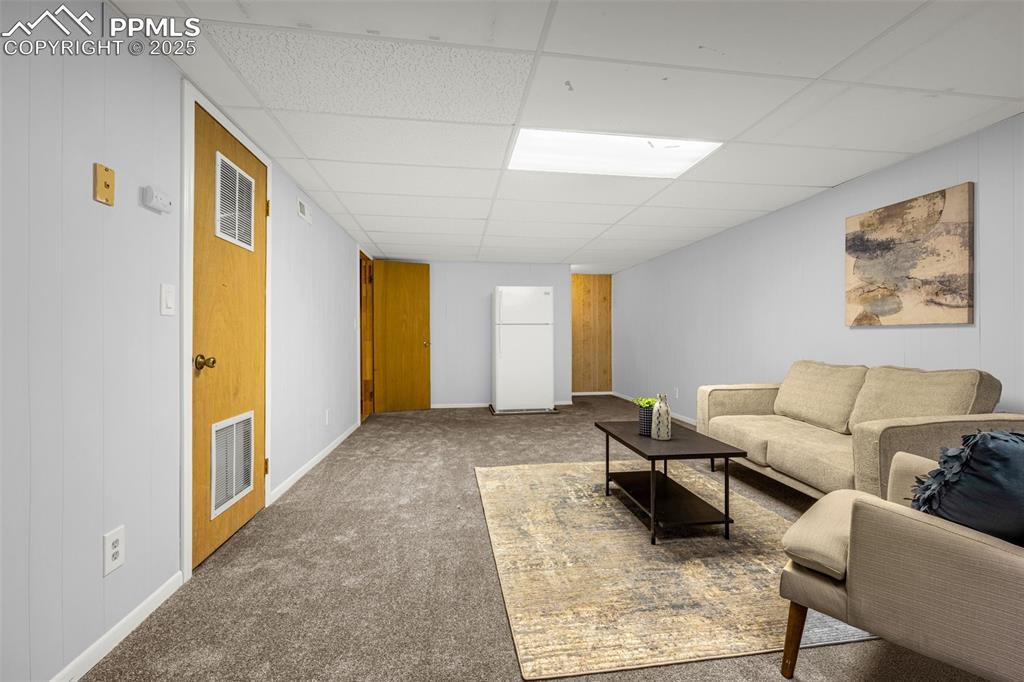 Image 27 of 40: Living room with carpet, a paneled ceiling, and baseboards