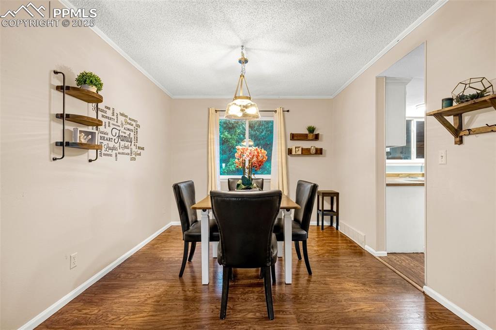 Image 5 of 40: Dining space featuring dark wood-style flooring, crown molding, and baseboa