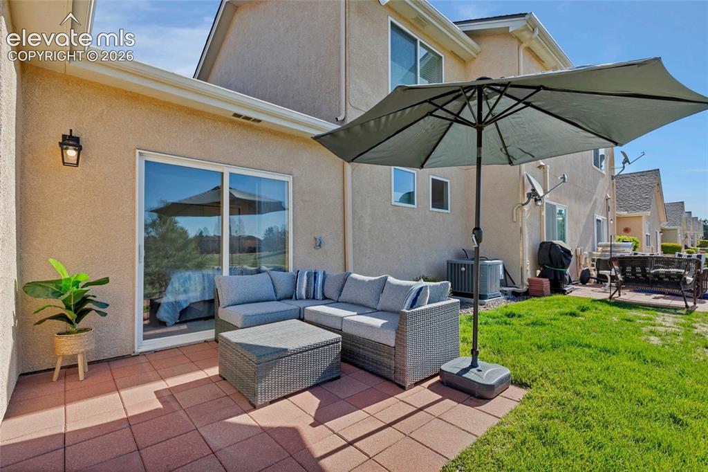 Image 23 of 26: The covered back patio with wicker sectional seating and a large umbrella c