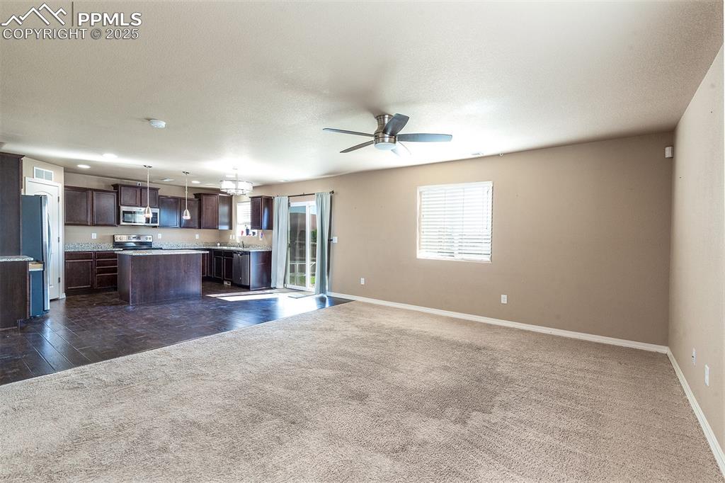 Image 11 of 33: Unfurnished living room with dark carpet, a ceiling fan, and a textured cei
