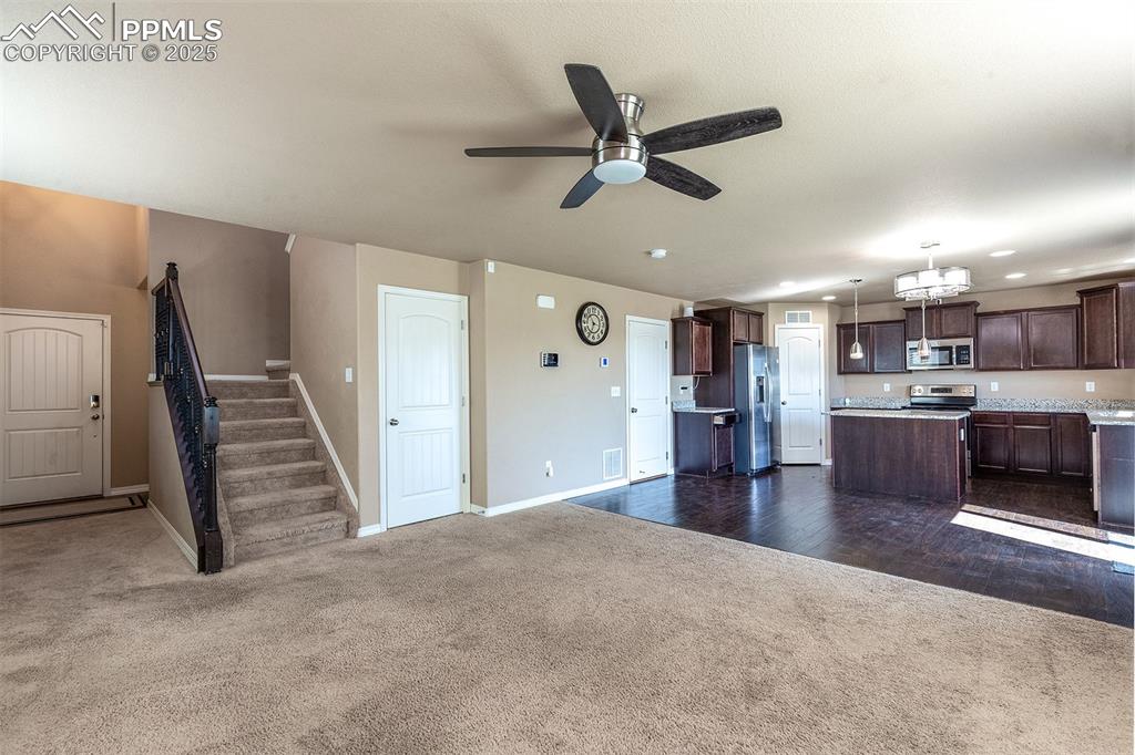 Image 12 of 33: Unfurnished living room with dark carpet, a ceiling fan, stairway, and dark