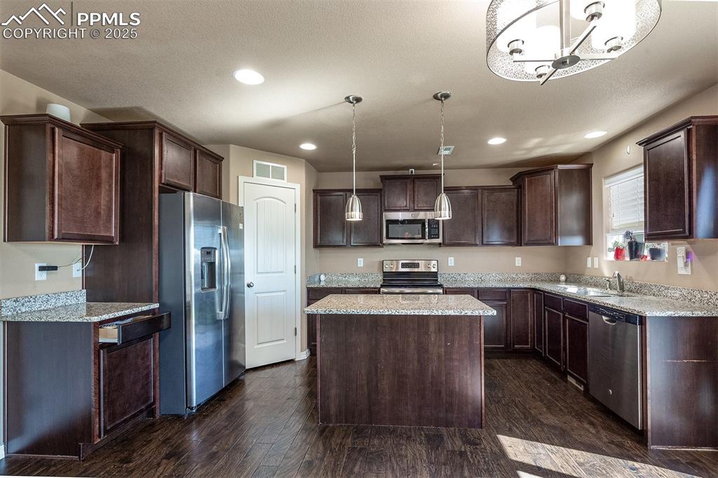 Image 13 of 33: Kitchen with dark brown cabinetry, stainless steel appliances, dark wood-st