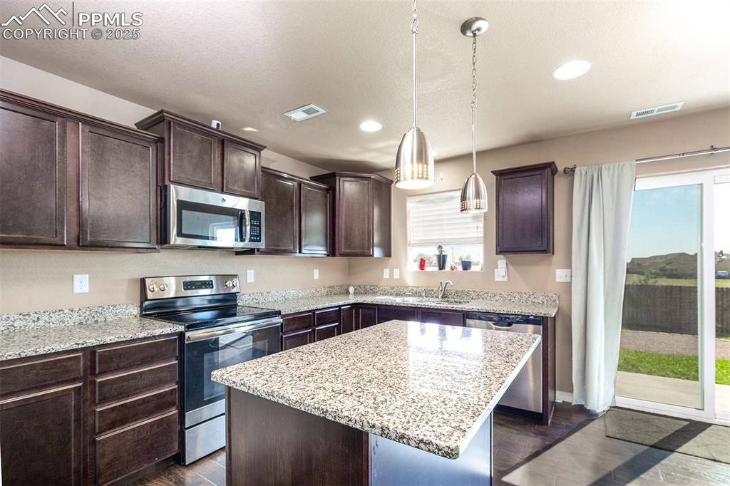 Image 16 of 33: Kitchen with dark brown cabinets, stainless steel appliances, a kitchen isl