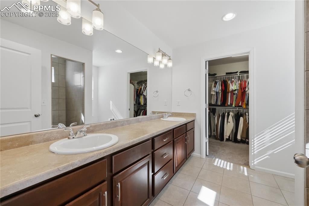 Image 14 of 37: Full bathroom with a walk in closet, light tile patterned floors, double va