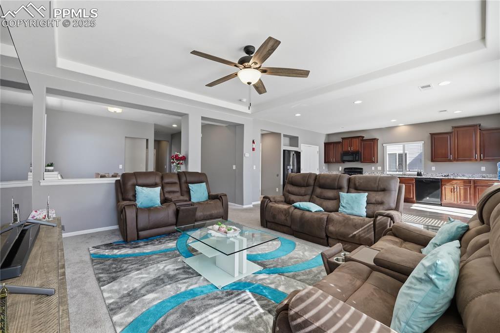 Image 7 of 37: Living area featuring carpet flooring, ceiling fan, a raised ceiling, and r