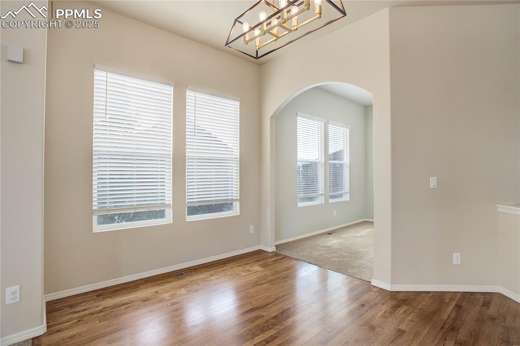 Image 24 of 43: Spare room with baseboards, arched walkways, a notable chandelier, and wood
