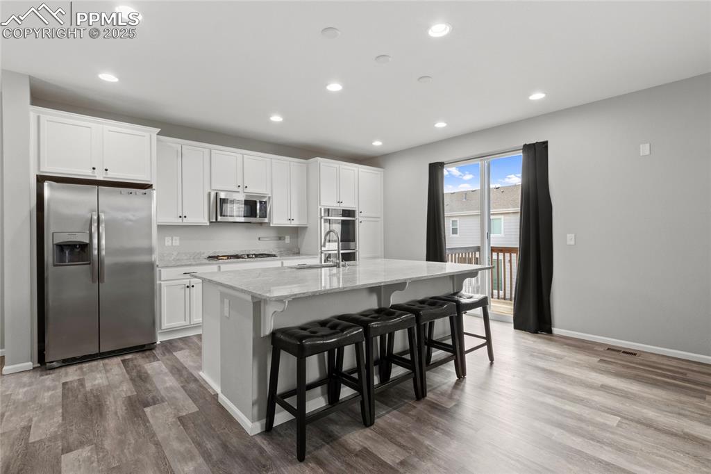 Image 11 of 44: Kitchen with stainless steel appliances, light stone counters, white cabine