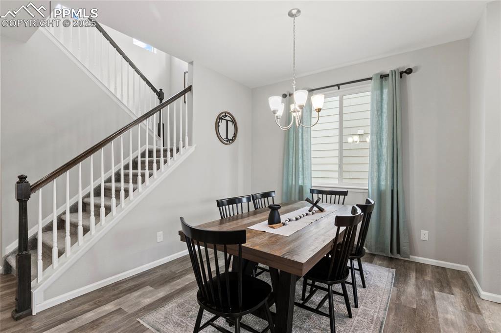 Image 13 of 44: Dining area with dark wood finished floors, a chandelier, and stairs