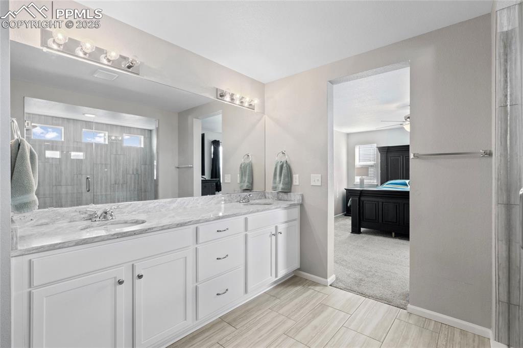 Image 22 of 44: Ensuite bathroom with double vanity, a stall shower, ceiling fan, and light