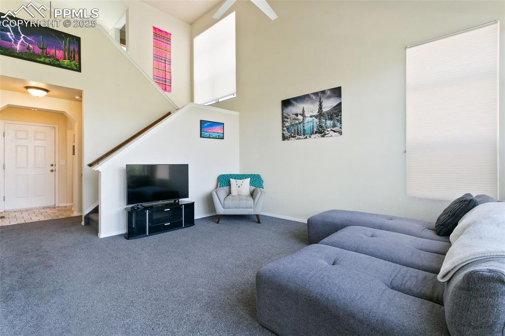 Image 10 of 29: Carpeted living room with stairs, a towering ceiling and view of entryway