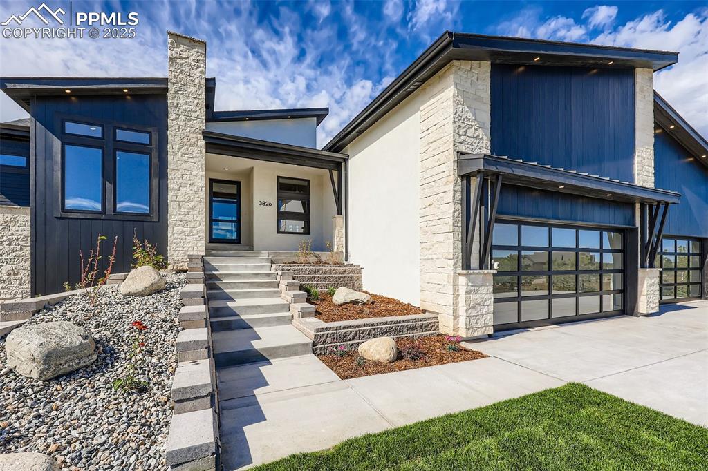 Image 2 of 41: Modern home with stone siding, covered porch, concrete driveway, and an att