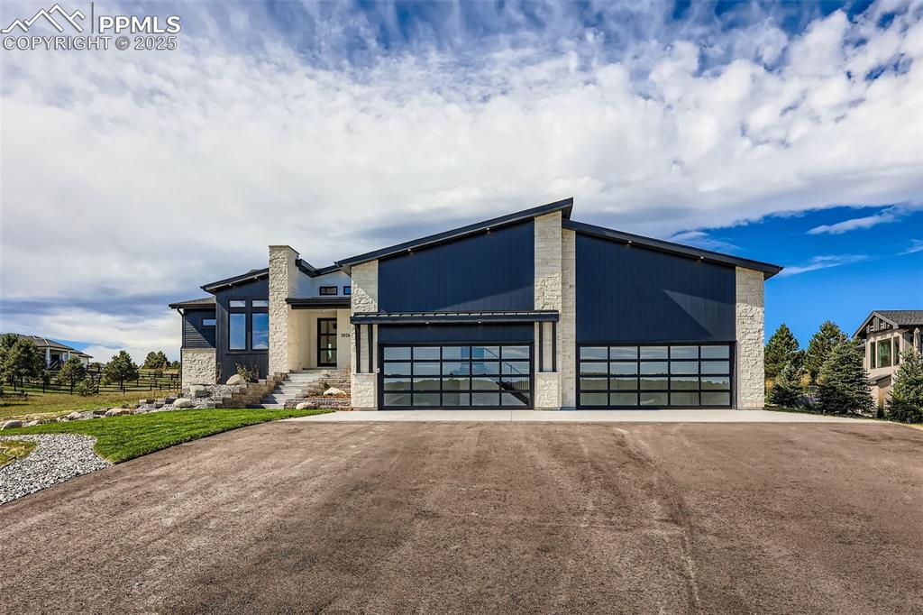 Image 3 of 41: View of front of property with stone siding, driveway, an attached garage,