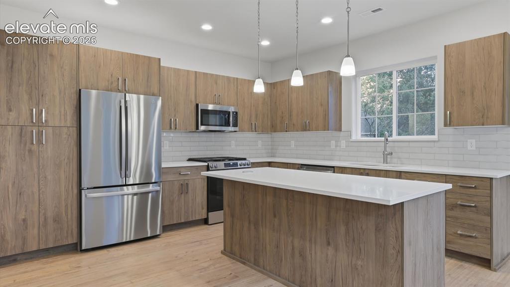 Image 40 of 50: Island Kitchen with breakfast bar, pendant lights, sleek cabinetry with qua