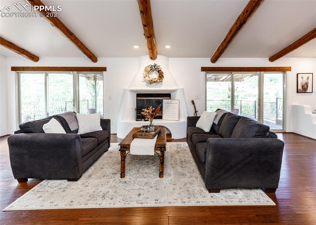 Image 11 of 50: Living area with dark wood-style floors, a large fireplace, and beamed ceil