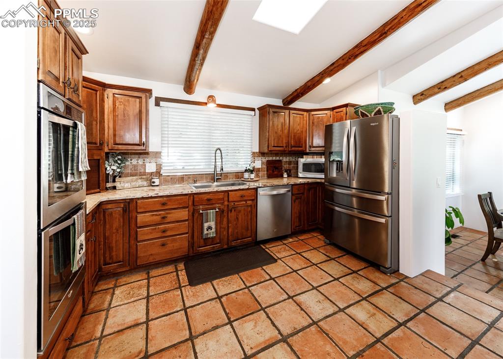 Image 15 of 50: Kitchen with backsplash, stainless steel appliances, and beam ceiling
