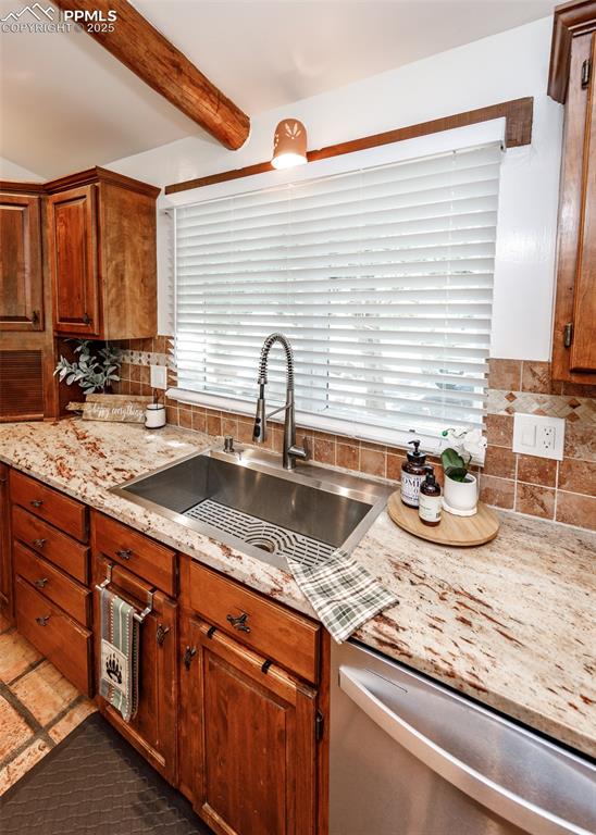 Image 16 of 50: Kitchen with tasteful backsplash, dishwasher, light stone counters, beamed 