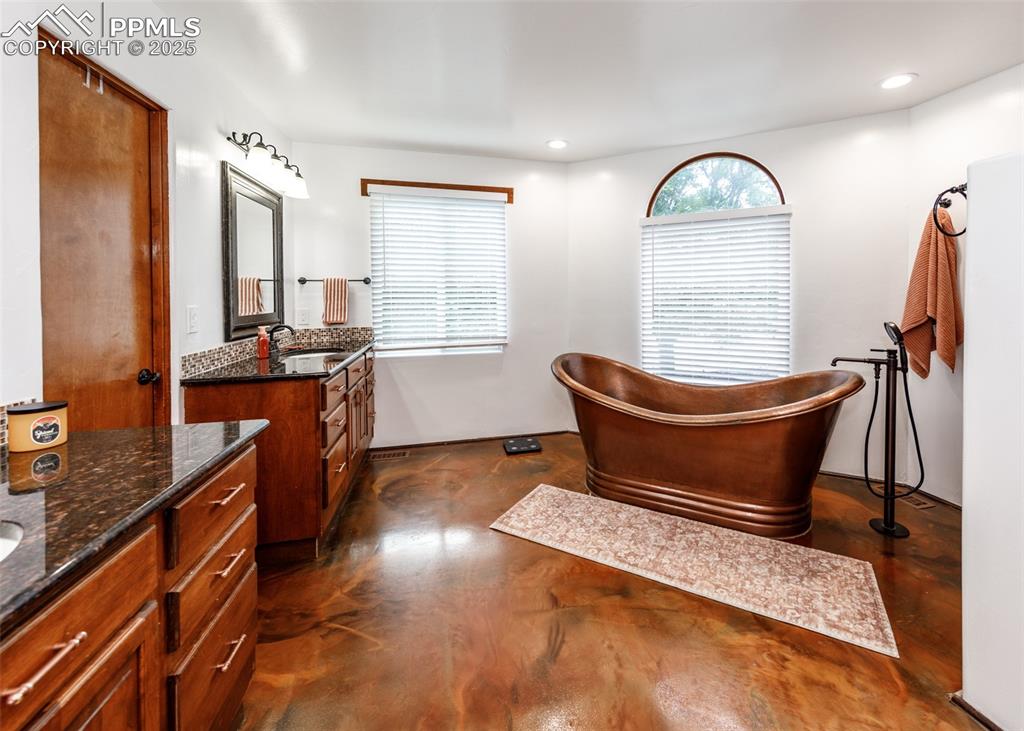 Image 24 of 50: Bathroom with two vanities, a freestanding tub, concrete floors, and recess