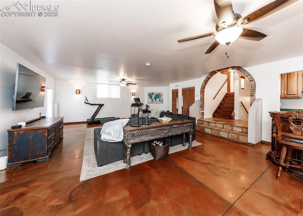 Image 27 of 50: Living area featuring a ceiling fan, finished concrete floors, and stairway