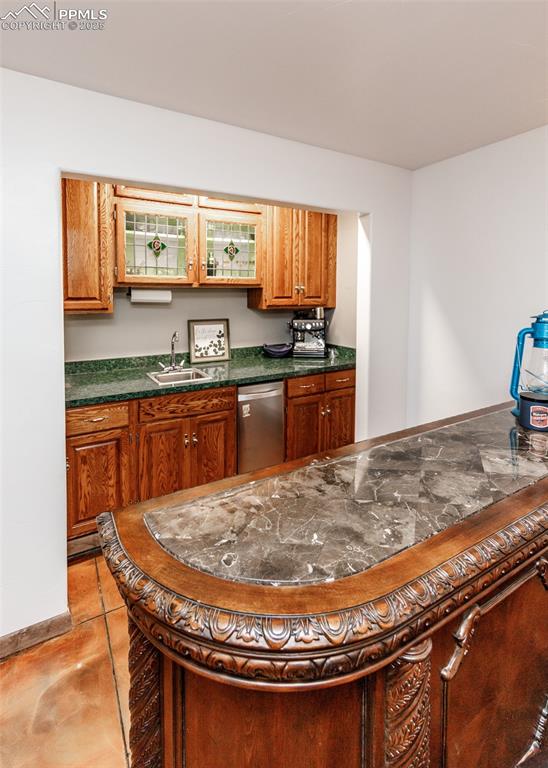 Image 29 of 50: Kitchen with dark countertops, brown cabinetry, stainless steel dishwasher,