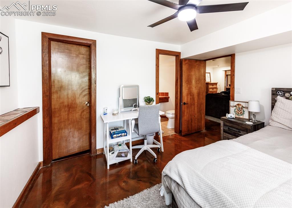 Image 34 of 50: Bedroom with finished concrete flooring, ceiling fan, a desk, and connected