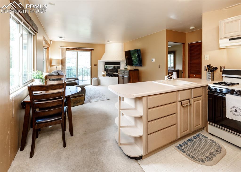 Image 40 of 50: Kitchen featuring a peninsula, white gas range, open shelves, and light cou