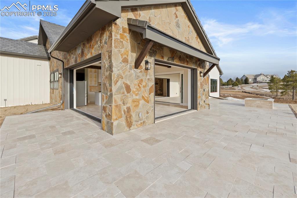 Image 13 of 47: Back of property featuring a patio area, a shingled roof, and stone siding