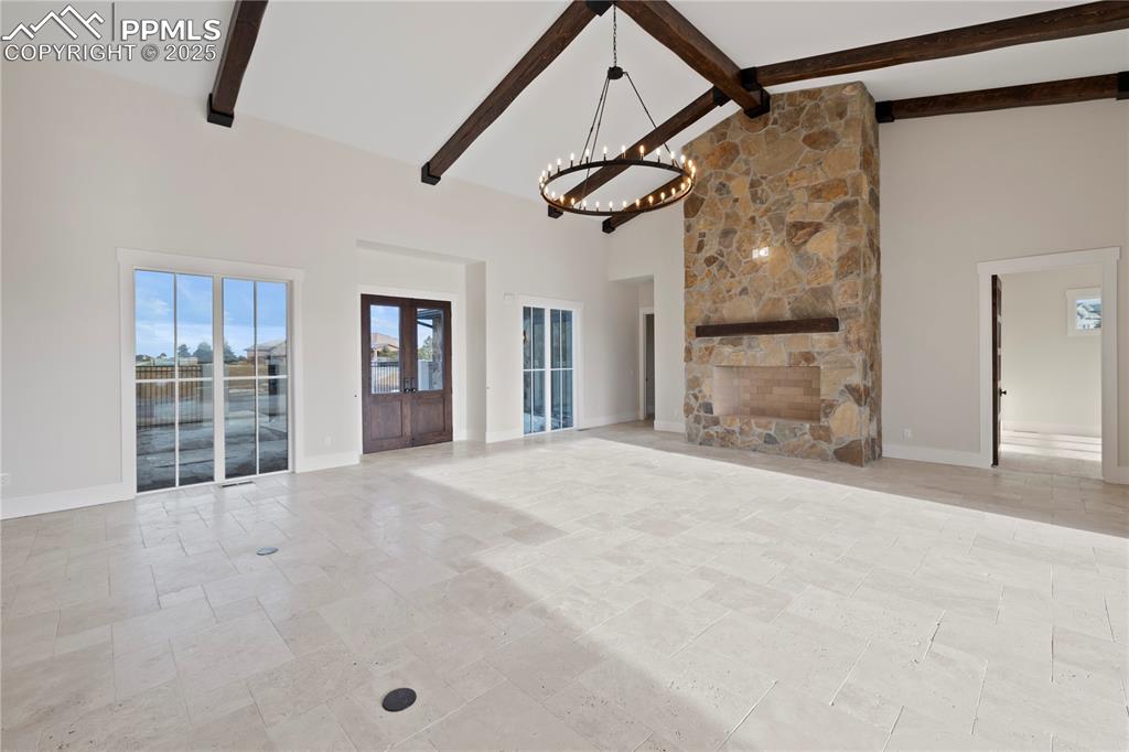 Image 17 of 47: Unfurnished living room with high vaulted ceiling, a chandelier, beamed cei