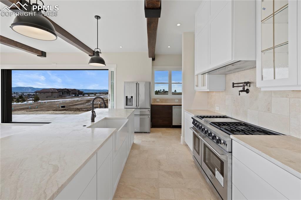 Image 22 of 47: Kitchen with decorative backsplash, beamed ceiling, appliances with stainle