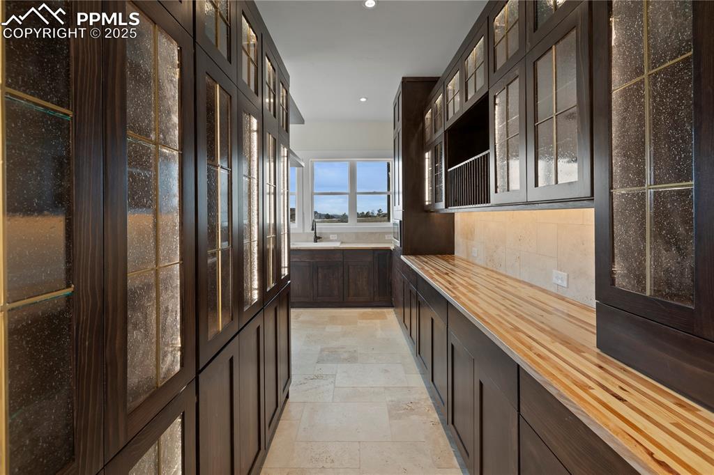 Image 26 of 47: Kitchen with dark brown cabinetry, stone tile floors, wooden counters, glas