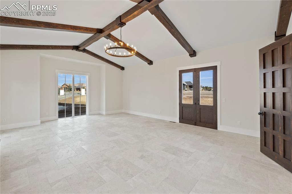 Image 28 of 47: Unfurnished living room with vaulted ceiling with beams, stone tile floors,