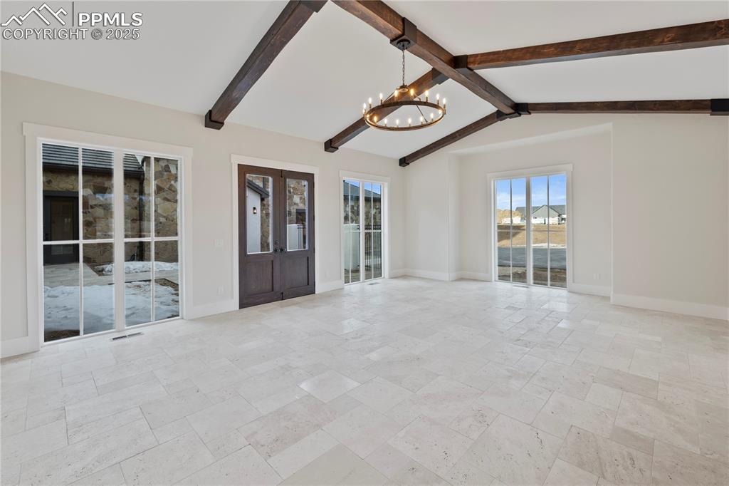 Image 31 of 47: Spare room with lofted ceiling with beams, visible vents, baseboards, stone
