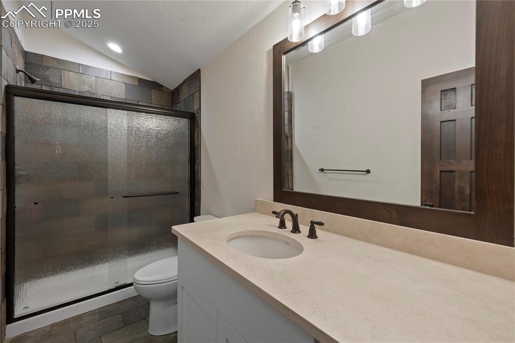 Image 45 of 47: Full bath featuring vanity, toilet, vaulted ceiling, and a shower stall