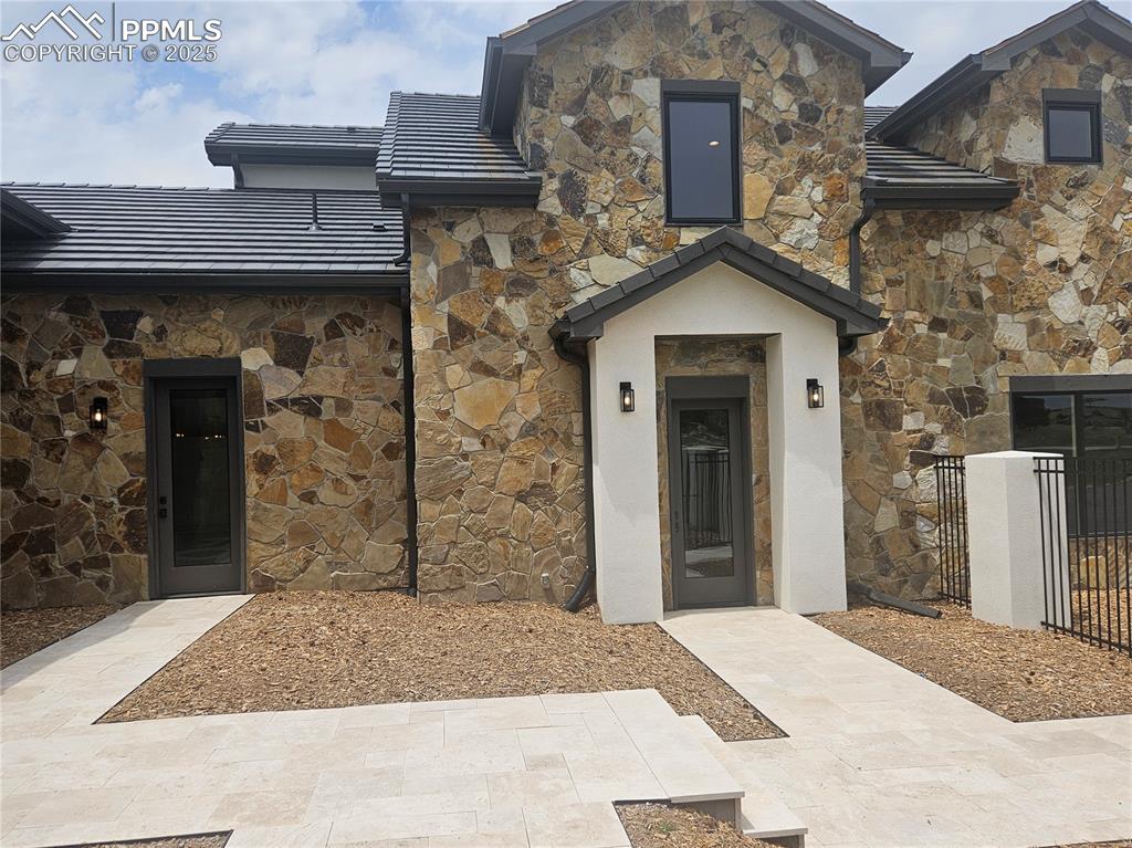 Image 5 of 47: View of exterior entry with stone siding, a tile roof, and stucco siding