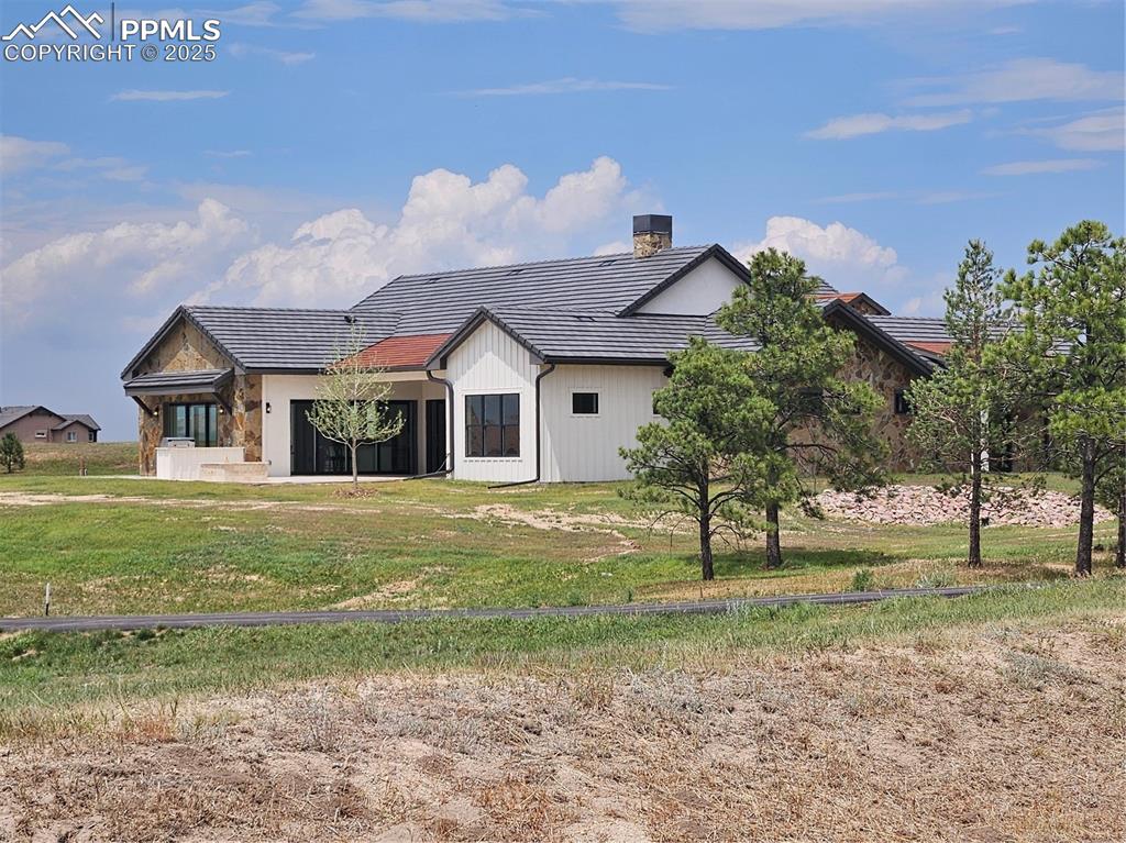 Image 7 of 47: Back of house with a tile roof, a chimney, a lawn, and stone siding