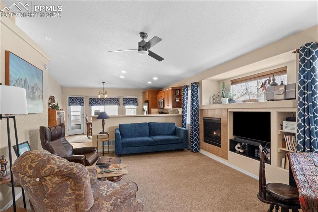 Image 8 of 37: Carpeted living room featuring ceiling fan with notable chandelier, a firep