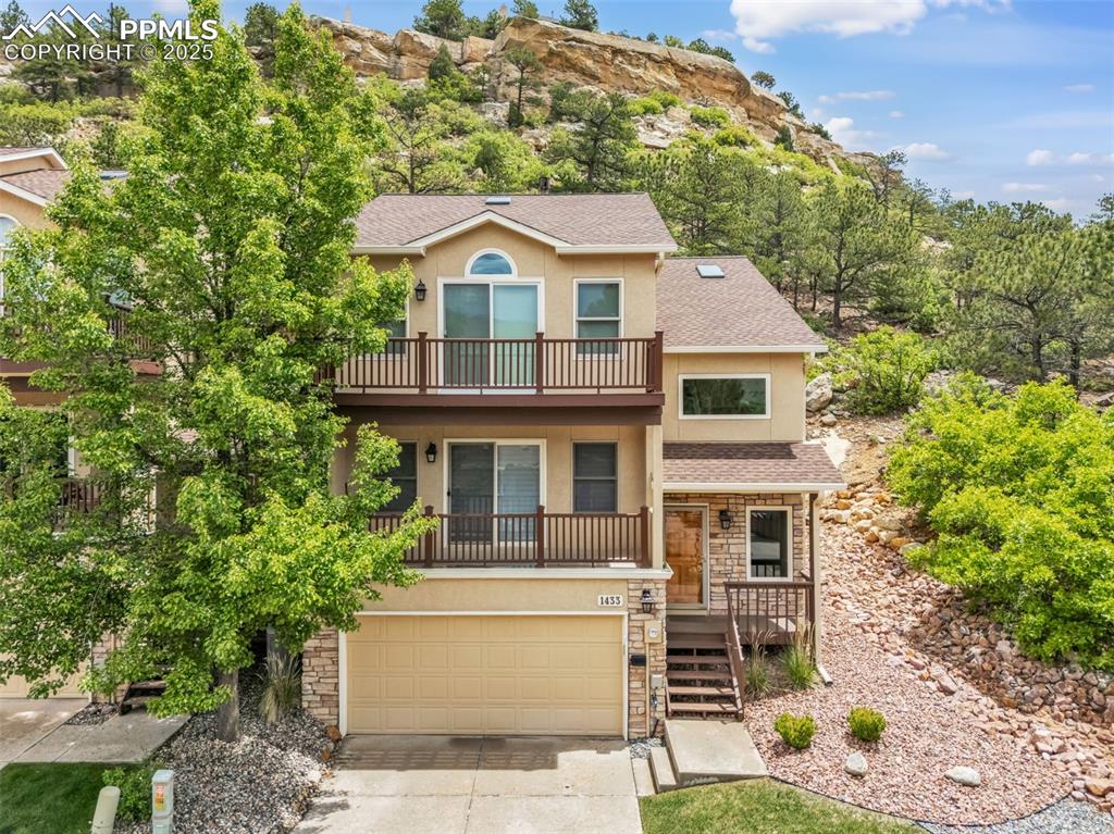 Caption: View of front of house with a balcony, stucco siding, stone siding, and concrete driveway
