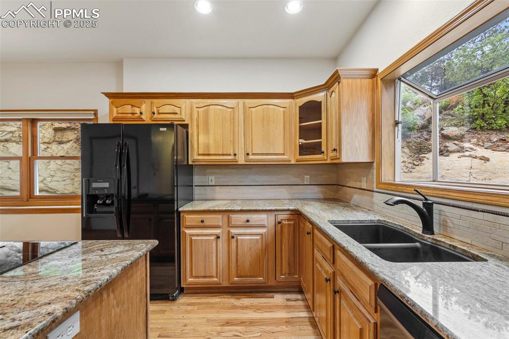 Image 13 of 48: Kitchen featuring black refrigerator with ice dispenser, a sink, light ston