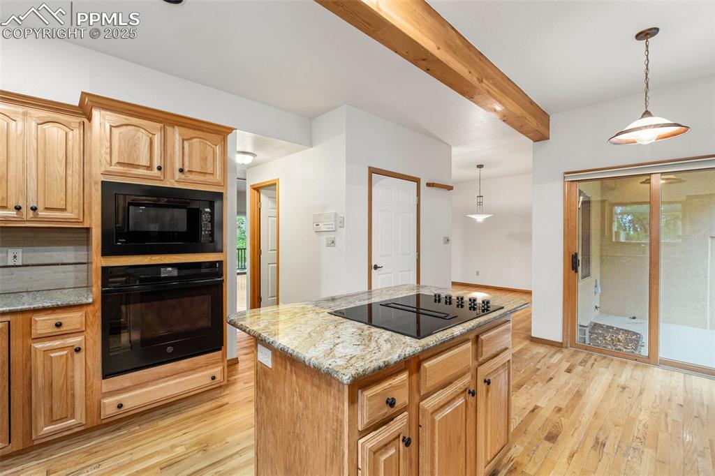 Image 15 of 48: Kitchen with black appliances, light wood finished floors, beamed ceiling,