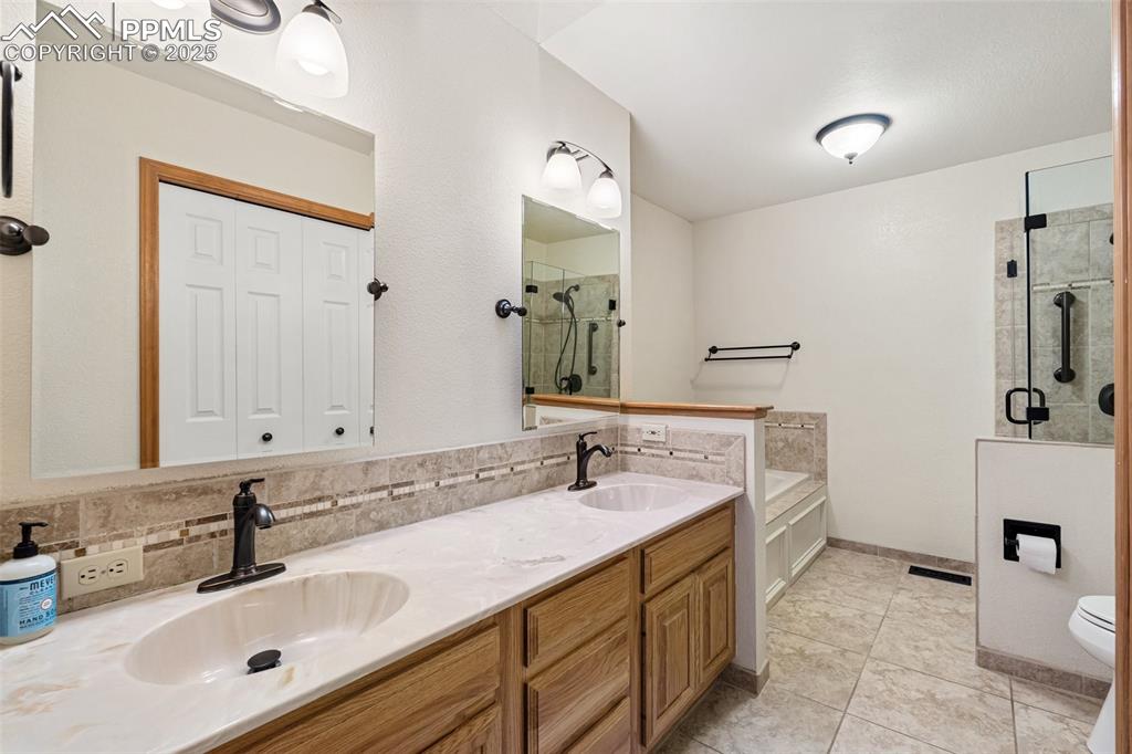Image 24 of 48: Bathroom with a shower stall, a garden tub, double vanity, toilet, and tile