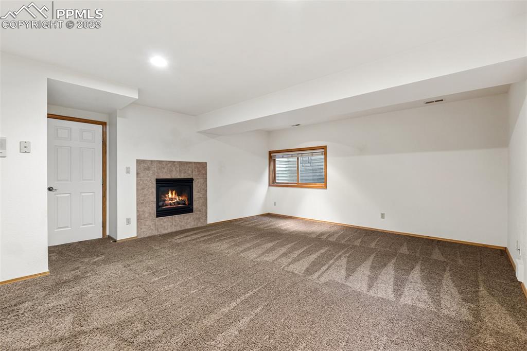 Image 42 of 48: Unfurnished living room with carpet floors, baseboards, a tiled fireplace,