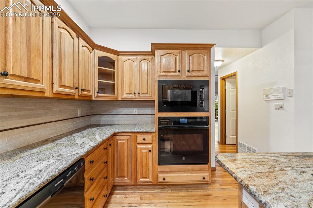 Image 9 of 48: Kitchen featuring black appliances, light stone counters, light wood-style